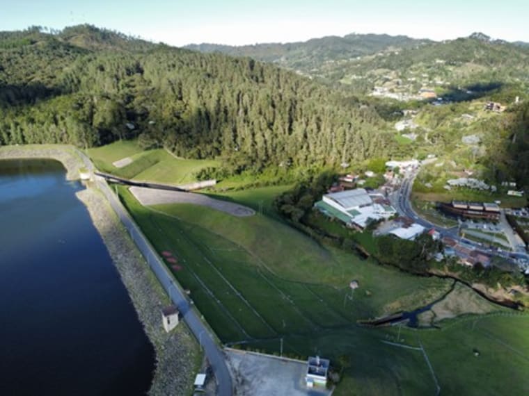 An aerial view of a reservoir and dam set in green hills.