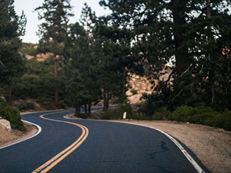 A winding two-lane road through a forest.